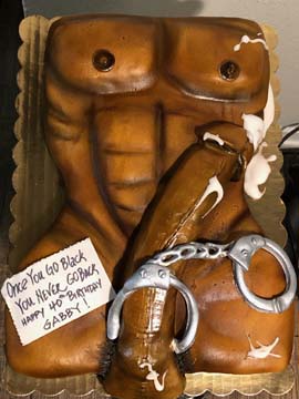 A cake shaped like a muscular male torso with abs, featuring a chocolate arm holding a fondant belt and handcuffs. A handwritten note says, Once you go black, you never go back. Happy 40th birthday Gabby!.