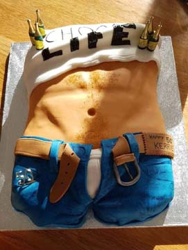 Novelty cake shaped like a mans torso wearing blue jeans and a white shirt with CHOOSE LIFE on it. The belt is partly undone, and small champagne bottles are on top.