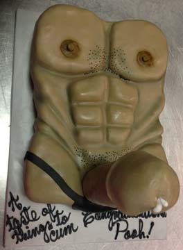 A novelty cake shaped like a male torso with defined abs. The cake includes details like nipples and a thong. The text on the cake board reads, A taste of things to cum. Congratulotions Posh!.