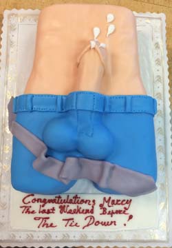 A cake shaped like a mans torso wearing blue pants and a belt, with visible belly and back. The cake has a humorous theme with icing messages.