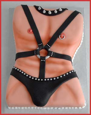 A cake shaped like a human torso, decorated with black fondant straps and studs resembling leather harnesses, depicting a provocative style. The cake has skin-toned icing and is bordered in red.